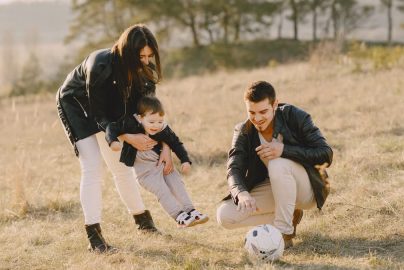 A happy family playing with a soccer ball in a grassy field on a sunny day.